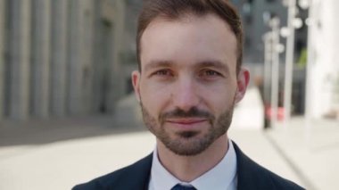Close-up portrait of smiling ceo executive looking to camera. Male businessman in 30s wearing classical suit posing outdoors on modern office building background