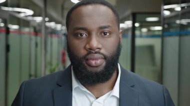 Close-up portrait of smiling african american businessman in formal suit standing in modern office corridor.