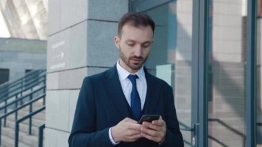 Cep telefonunda uygulama kullanan yakışıklı sakallı iş adamı. Resmi takım elbiseli genç adam mesajlaşıyor, akıllı telefonuyla sohbet ediyor şehir merkezinde yürürken..