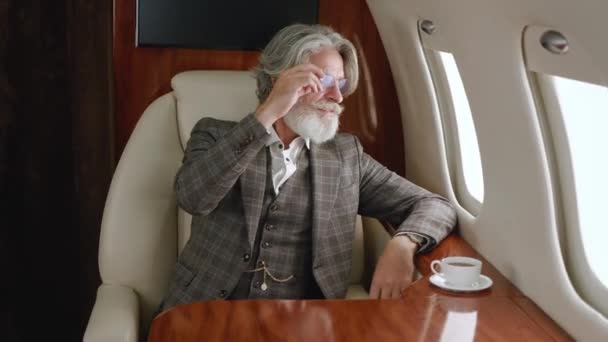 Stylish mature millionere man wearing classical suit luxury flying in private airplane. Confident CEO businessman looking through corporate jet window. Luxury traveling in private jet. — Stock Video