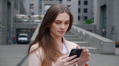 Şehir caddesinde cep telefonuyla yazı yazan iş kadınının portresi. Şehir merkezindeki ofis binasının yakınında akıllı telefon kullanan kadın yönetici.