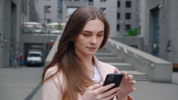 Şehir caddesinde cep telefonuyla yazı yazan iş kadınının portresi. Şehir merkezindeki ofis binasının yakınında akıllı telefon kullanan kadın yönetici. — Stok video