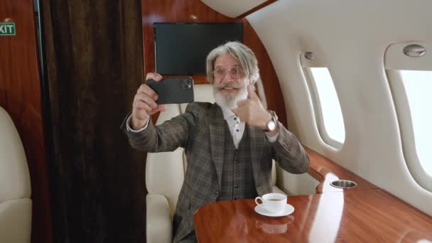 Homme riche mature utilisant un smartphone pour les appels vidéo pendant un voyage en jet privé de luxe. Gris cheveux élégant homme âgé ayant visioconférence sur avion — Video