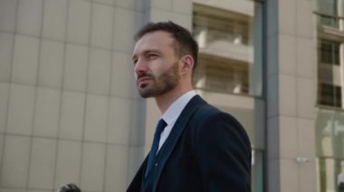 Şehir merkezinde kendine güvenen bir CEO 'nun sabit çekimi. 30 'lu yaşlarda, modern ofis arka planında açık hava pozu veren klasik takım elbiseli bir iş adamı.