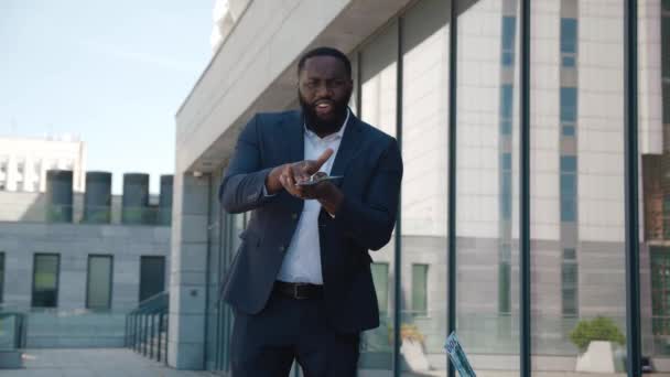 Exitoso empresario afroamericano con traje que arroja dinero a la cámara de pie al aire libre cerca del edificio de oficinas. Lluvia de dinero, cayendo dólares. Concepto de negocio exitoso. — Vídeo de stock