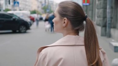Şehir merkezinde yürüyen beyaz ceketli bir kadının arka görüntüsü. Arka planda, işe gidip gelen genç bayan çalışanların arka planda bulanık insanlar, yoğun şehir hayatı.