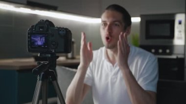 Mutlu blogcu adam evde profesyonel kamerayla video kaydediyor. Erkek içerik yaratıcısı kanepede oturup online dersler çekiyor. Vlog kaydedicisi video kamera ile vlog kaydediyor