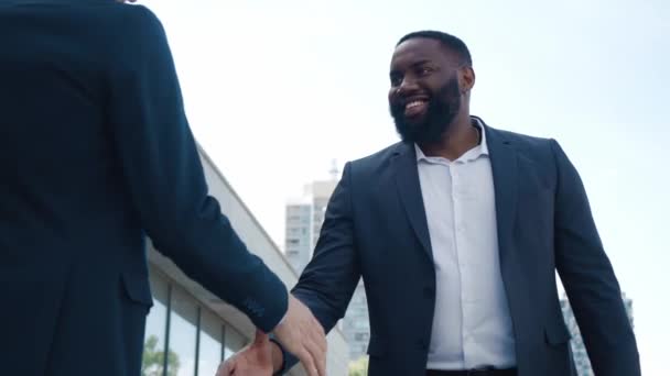 Lövöldözés afro-amerikai és kaukázusi férfi kollégák formalwear kezet rázva és megvitatása üzleti miközben áll a szabadban közelében üzleti központ — Stock videók