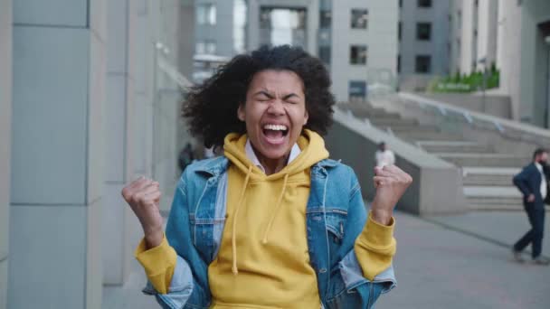Opgewonden Afrikaans amerikaanse jonge vrouw in jean jas maken winnaar gebaar met twee handen en schreeuwen vieren succes te winnen, buiten in het centrum — Stockvideo
