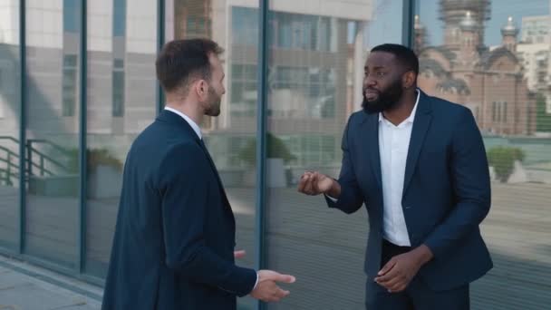 Dva naštvaní obchodníci, kteří se hádají o konflikt, stojí venku u kancelářské budovy. Dva naštvaní muži v oblecích zuřivě křičí a nadávají si. — Stock video