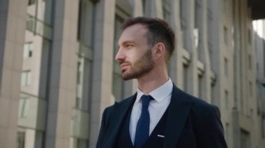 Şehir merkezinde duran kendine güvenen CEO 'nun portresi. 30 'lu yaşlarda erkek işadamı klasik takım elbise giyiyor ve modern ofis arka planında dışarıda poz veriyor.