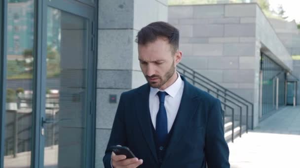 Knappe bebaarde zakenman in het gebruik van app op zijn mobiele telefoon. Jongeman in formele pak sms 'jes, chatten op zijn smartphone tijdens het lopen in het centrum van het kantoor district. — Stockvideo