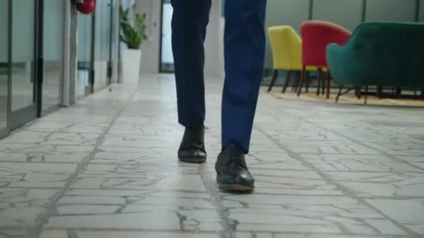 Açık uzay ofis koridorunda yürüyen tanınmayan bir erkek girişimcinin ön ayakları. Resmi takım elbiseli iş adamının bacakları ofis koridorunda yürüyor.. — Stok video
