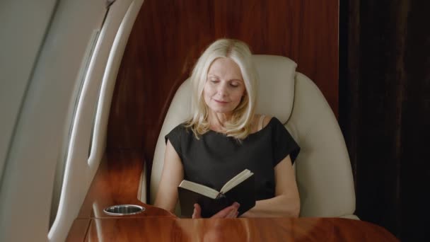 Piękna dojrzała bogata kobieta czyta książkę lub notatnik podczas lotu w prywatnym samolocie. Luksusowe podróże prywatnym odrzutowcem. — Wideo stockowe
