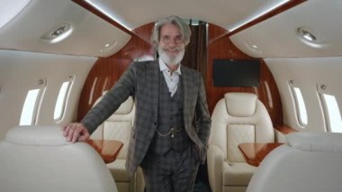 Özel uçakta duran, klasik takım elbiseli, şık, yaşlı bir milyonerin portresi. Gülümseyen sakallı CEO iş adamı şirket jetine bakıyor. Özel jetle seyahat eden lüks..