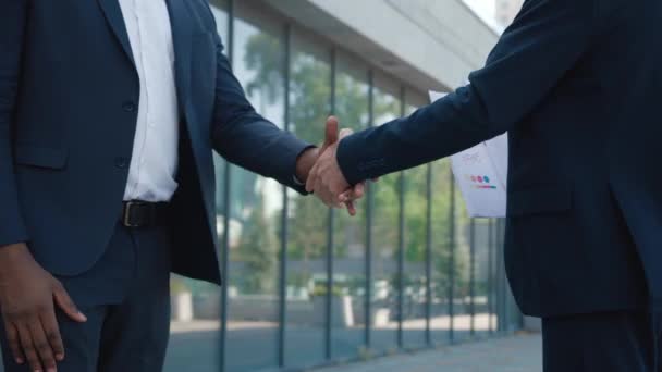 Primo piano di due colleghi, uomini africani e caucasici in abiti formali, che si stringono la mano all'aperto nel business center. Uomini d'affari maschi si incontrano. Incontro dei partner. — Video Stock