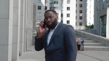 Kızgın Afro-Amerikalı iş adamı cep telefonuyla konuşuyor, iş yerinde dışarıda duruyor. Dışarıda ciddi bir konuşma yapan deli Afrikalı profesyonel erkek portresi..