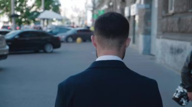 Kendine güvenen bir adamın şehir merkezindeki cadde boyunca yürüyüp şehir merkezindeki arka plandaki işlere bakması. İş adamlarının takım elbise giyip işe gidiş gelişlerinin arkası..