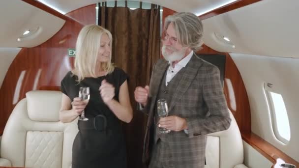Happy mature rich couple dancing while luxury traveling in private jet plane. Senior man and woman enjoying vip romantic traveling with glasses of champagne, while flying on first class airlines — Stock Video