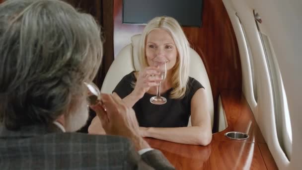 Зрелая богатая пара, путешествующая на частном самолете. Старший мужчина и женщина наслаждаются VIP романтические путешествия с бокалами шампанского, глядя в окно во время полета на авиакомпании первого класса — стоковое видео