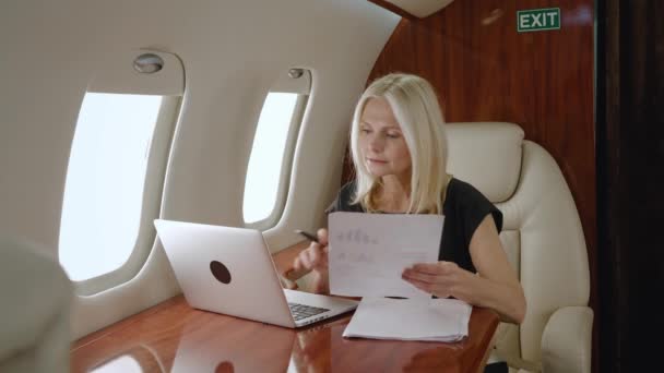 Bohatá vyspělá podnikatelka pracující s grafy, obchodními papíry a notebookem, studuje růstovou strategii společnosti během služební cesty soukromým letadlem nebo letadlem první třídy — Stock video