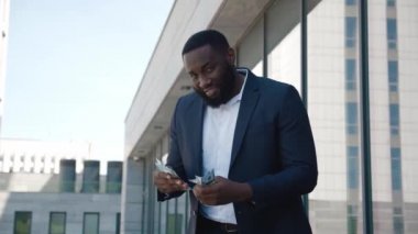 Başarılı bir Afrikalı işadamı dışarıda para sayıyor. Kendine güveni tam bir Afro-Amerikan erkeği bir deste dolara bakıyor ve gülümsüyor. Zenginlik ve başarı.