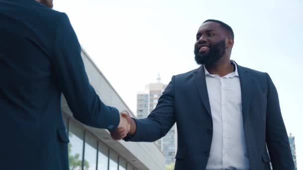 Mediana toma de dos hombres de negocios multiétnicos con elegantes trajes de pie juntos al aire libre, hablando y estrechando la mano en el centro de la ciudad — Vídeo de stock