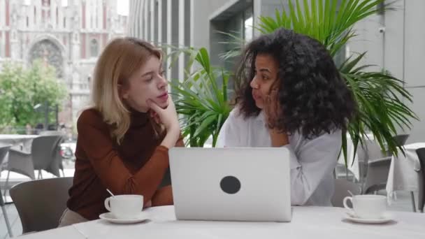 Jóvenes amigas trabajando juntas con computadora portátil en la cafetería al aire libre — Vídeo de stock