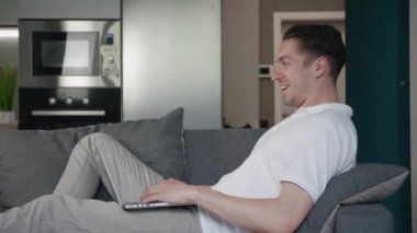 Mutlu genç adam başarıyı kutluyor online bahsi kazanıyor ve EVET hareketi gösteriyor. Şanslı erkek serbest yazar internette harika haberler okuyor. Evdeki rahat koltukta dinlenirken dizüstü bilgisayar kullanıyor..