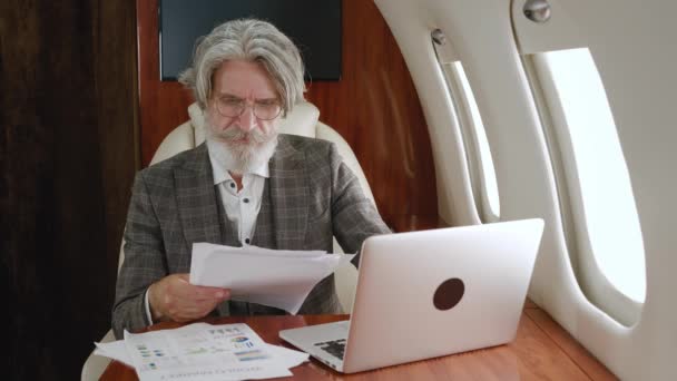 Rušný zralý podnikatel pracující s dokumenty a pomocí notebooku při letu na soukromém tryskovém letadle. — Stock video