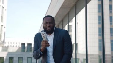 Açık havada para dolu bir paketle başarılı bir Afro-Amerikan iş adamının portresi. Kendine güvenen mutlu girişimci bir tomar dolar gösteriyor. Zenginlik ve başarı.