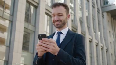 Modern Office Binası 'nın yakınlarındaki Smartphone kullanan gülümseyen iş adamının portresi. Klasik takım elbise giyiyordu. Sosyal ağ. Uygulamalar. Akıllı telefonlar.