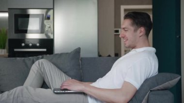 Mutlu genç adam başarıyı kutluyor online bahsi kazanıyor ve EVET hareketi gösteriyor. Şanslı erkek serbest yazar internette harika haberler okuyor. Evdeki rahat koltukta dinlenirken dizüstü bilgisayar kullanıyor..