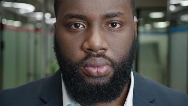 Retrato de perto de um sério empresário barbudo afro-americano no corredor de um prédio de escritórios. Chefe masculino confiante olhando ambiciosamente para a câmera, no fundo de um escritório moderno — Vídeo de Stock