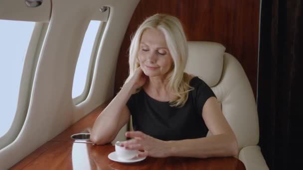 Piękny sukces dojrzała kobieta biznesu podróżuje prywatnym samolotem. Portret bogatej seniorki pijącej herbatę lub kawę podczas luksusowej podróży liniami lotniczymi pierwszej klasy biznesowej — Wideo stockowe