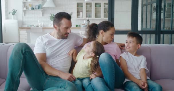 Két generációs család pihen a kanapén a kényelmes nappaliban. A szülők kedvesek kommunikálnak az utódaikkal. Gyermekvédelem és boldog családi kapcsolatok fogalmai. — Stock videók
