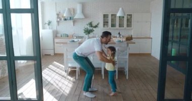 Mutlu ve sevgi dolu bir babanın uzun bir portresi güzel kızını elinden tutar ve etrafında döndürür, mutfakta dans eder. 4K video kaydı.
