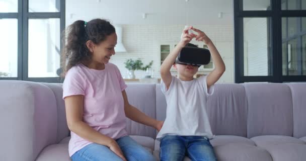 A spanyol nő ránéz a fiára, aki virtuális valóság szemüveget visel. VR-koncepció. A meghökkent és izgatott fiú aktívan megérinti a levegőt egy virtuális valóság élmény során. 4 K videoanyag — Stock videók