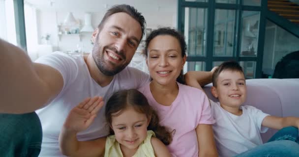 Από την άποψη της εικόνας του οικογενειακού πορτραίτου με όμορφο άνδρα, πατέρα, σύζυγο να κάθεται δίπλα στην όμορφη σύζυγό του και τα χαριτωμένα παιδιά του, κρατώντας ένα κινητό τηλέφωνο και έχοντας οικογενειακή βιντεοδιάσκεψη πάνω από μια βιντεοκλήση. — Αρχείο Βίντεο