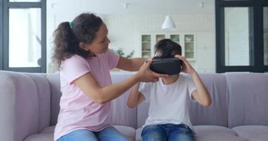 Afrikalı Amerikalı kadın oğluna sanal gerçeklik gözlüğü takıyor. Smartphone, VR kulaklığı kullanıyor. Sanal Gerçeklik Konsepti. Harika bir çocuk sanal gerçeklik deneyimi sırasında havaya dokunuyor. 4 K video kaydı