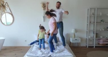 Yatak odasındaki yatakta dans eden sevimli melez bir ailenin 4K görüntüleri. Sevimli çocuklar babaları ve Afrikalı Amerikalı anneleriyle eğleniyor.