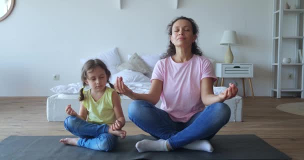Calm woman sitting next to her daughter in lotus position on fitness mat and meditating together, doing correct breathing technique. Yoga, family meditation concepts. Healthy lifestyle. 4K video — 비디오