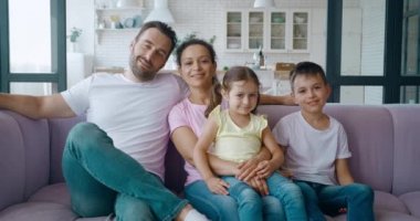 İki melez çocuklu İspanyol kadın, kocasının yanına oturmuş, kafasını kanepeye yaslıyor, kameraya tatlı tatlı gülümsüyor. Mutlu çok ırklı ailenin 4K video portresi