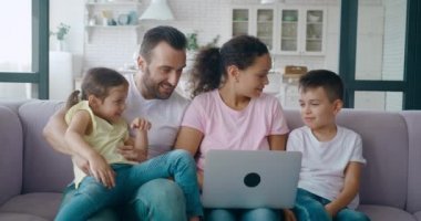 Babası kızına sarılırken annesi dizüstü bilgisayarla tavsiye için oğluna dönüyor. Aile online alışveriş, rezervasyon, bilet ve otel rezervasyonları hakkında seçimler yapar.