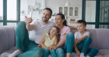 Melez etnik kökenli mutlu bir aile, video görüşmesi sırasında babalarının elindeki akıllı telefon ekranına bakarak selamlaşır. Cep telefonuyla aile video konferansı