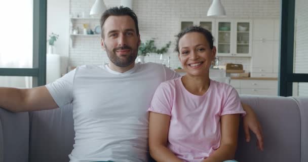 Vídeo 4K. Retrato de casal close-up confiante de encantador marido e mulher de meia-idade sentados perto uns dos outros no fundo da cozinha, abraçando e sorrindo olhando para a câmera — Vídeo de Stock
