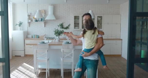 4K de un joven padre guapo está bailando en la cocina con su hija sentada en sus brazos. Concepto de paternidad, paternidad, ocio familiar. Amor, ternura y afecto — Vídeos de Stock