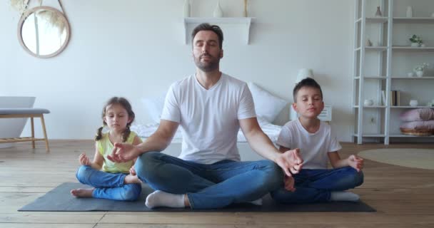 Красивый отец сидит в позе лотоса с очаровательными детьми по бокам, медитируя в тихой спокойной обстановке. Йога, медитация, здоровый ум, правильная техника дыхания. Счастливого отцовства. — стоковое видео