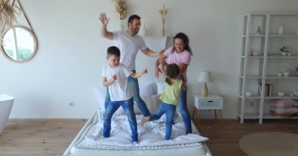 Família encantadora dançando na cama no quarto no belo dia ensolarado. Crianças bonitos se divertindo com seus pais alegres. — Vídeo de Stock