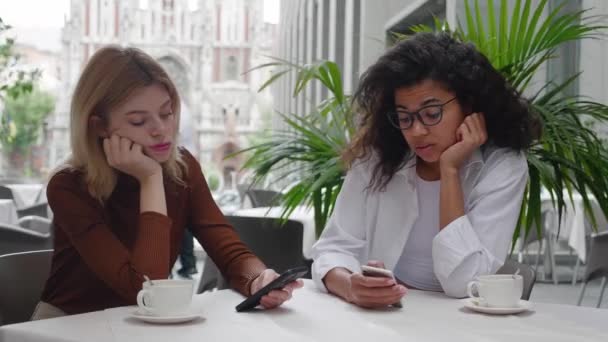 2人の退屈な女性の友人は、屋外カフェでスマートフォンでインターネットを閲覧した後. — ストック動画